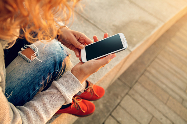 Rothaarige Frau sitzt auf einer Mauer und betrachtet ihr Smartphone